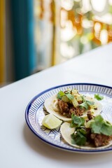 Tacos with fried chicken, spicy pineapple salca and cilantro. Plate of mexican food on a white table. Cafe interior in blur on the background    