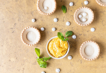 Empty shortbread tartlets, lemon curd, mini meringues and mint, concrete background. Process making dessert. Top view.