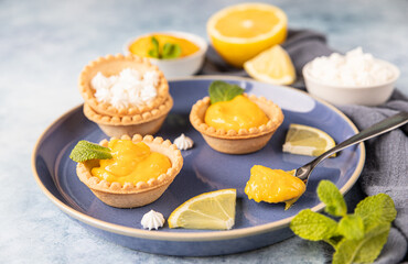 Obraz na płótnie Canvas Lemon curd mini tarts decorated with mint and lemon slices on blue plate.