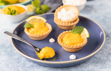 Obraz na płótnie Canvas Lemon curd mini tarts decorated with mint and lemon slices on blue plate.