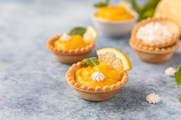 Mini tarts with lemon curd, mini meringue, lemon slices and mint, blue concrete background. - obrazy, fototapety, plakaty