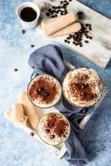 Traditional Italian dessert tiramisu in glass, light stone background. Coffee flavored portion dessert made of ladyfingers and mascarpone with cocoa powder.