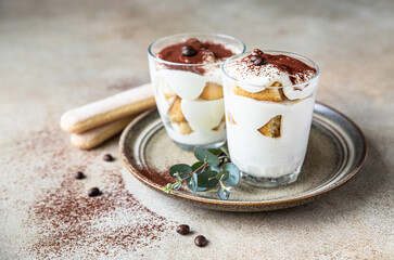 Traditional Italian dessert tiramisu in glass, light stone background. Coffee flavored portion dessert made of ladyfingers and mascarpone with cocoa powder.