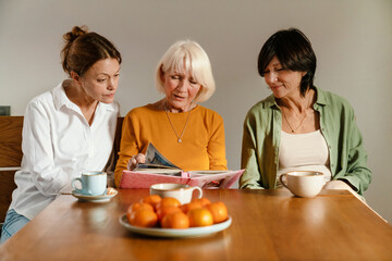 Mature three women talking and looking at photo album together