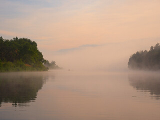 fog over the river at sunset a fisherman in a boat on the water
