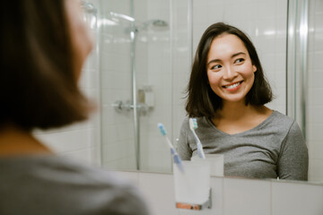 Young smiling asian girl standing in front of a mirror