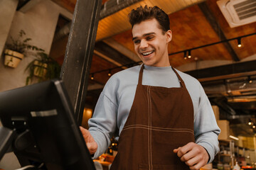 Young white waiter man wearing apron registering payment in cafe