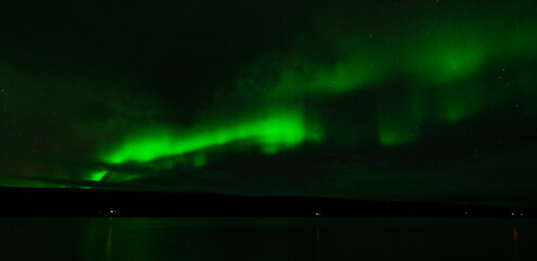 Northern lights over the plain lake with green lights