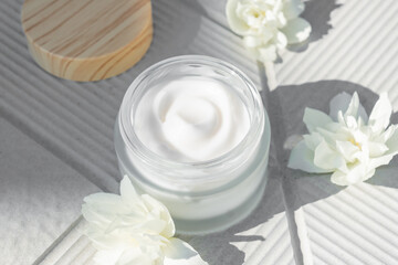 Fototapeta na wymiar Spa concept. Cream in a glass jar with jasmine flowers on whiteconcrete background. copy space. Close-up.