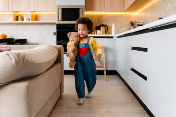 Little cute african curly boy hugging teddy bear while walking