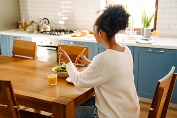 Back view of african woman sitting by table eating salad