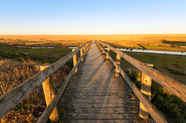 Fototapeta na wymiar Wooden bridge leading to Chesil Beach on a sunny morning with clear blue sky and hill of pebbles. 