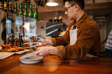 Adult asian man holding plate with croissant at counter in cafe