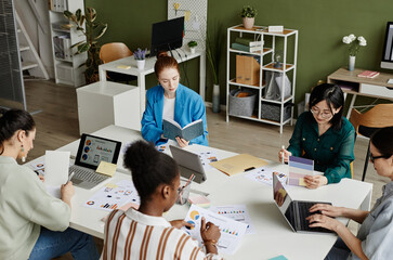 High angle view of multiethnic group of young female colleagues sitting at the same table and working with documents and gadgets