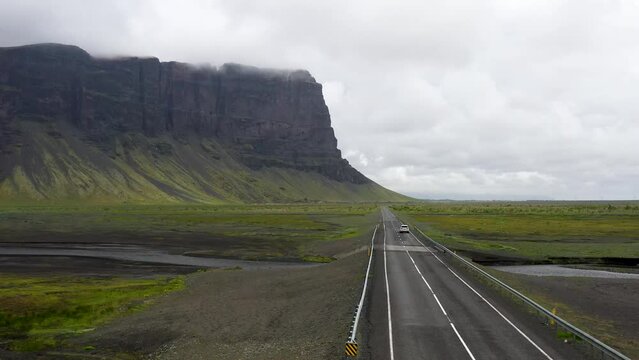 Car driving in Iceland on Ring Road through mountains with drone video moving up.