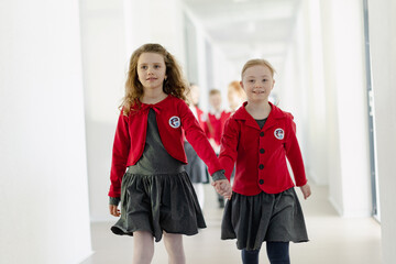 Happy schoolgrirl with Down syndrome in uniform holding hands with her classmate walking in scool...