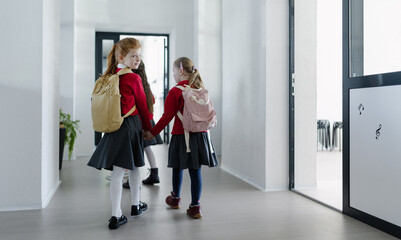 Happy schoolgirl with Down syndrome classmate in uniform walking in scool corridor with classmates,...