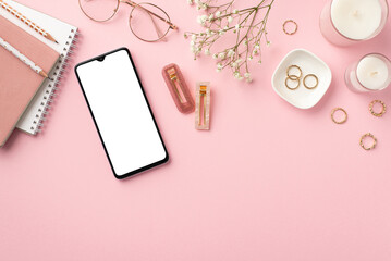 Fototapeta na wymiar Business concept. Top view photo of workplace smartphone candles diaries pencils stylish glasses gold rings trendy barrettes and white gypsophila flowers on isolated pastel pink background