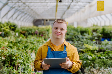 Young man with Down syndrome working in garden centre, holidng clipboard and checking plants.