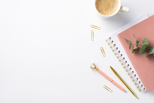 Business concept. Top view photo of workspace pink notebooks cup of hot drinking clips stylish pens and eucalyptus sprig on isolated white background with empty space