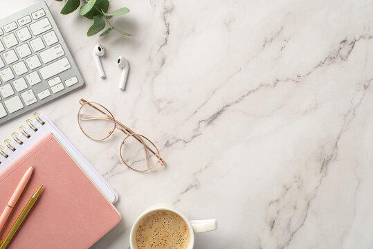 Business concept. Top view photo of workplace keyboard pink planners stylish glasses wireless earbuds pens cup of coffee and eucalyptus on white marble background with copyspace