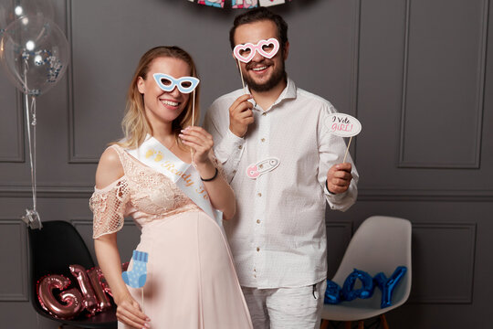 Front image of a smiling couple holding inscription boy or girl during gender reveals party, over props and balloons.