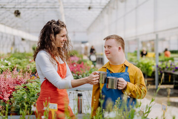 Woman florist with her young colleague with Down syndrome having tea break in garden centre.