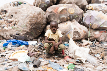 Young Africanboy sitting in front of huge bags full of sorted recyclable plastic bottles at a...