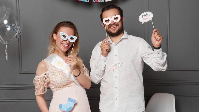 Front image of a smiling couple holding inscription boy or girl and mask on face during gender reveals party.