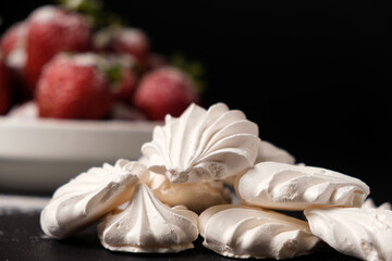 Meringue close up and strawberries in a plate on a black background. Fruit desserts.