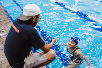 Latin swimming man trainer with chronometer talking some advices to teenagers swimmers students at...