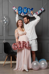 Full length image of a amused couple holding inscription boy or girl during gender reveals party, over balloons.
