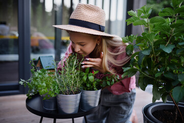 Young woman taking care of her herbs and smelling thme on terrace in tiny house, sustainable living.