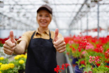 Selective focus of woman in flower greenhouse showing thumbs up