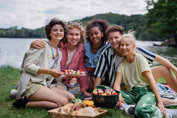 Group of multiracial young friends camping near lake and and having barbecue together, looking at camera.
