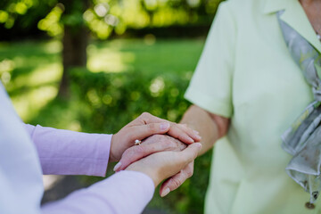 Close-up of caregiver consoling senior woman and touching her hand in park in summer.