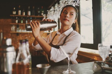 Beautiful Asian woman in gray apron preparing cocktail on the bar counter