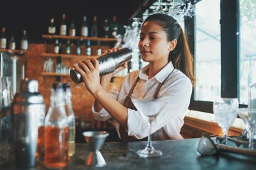 Beautiful Asian woman in gray apron preparing cocktail on the bar counter