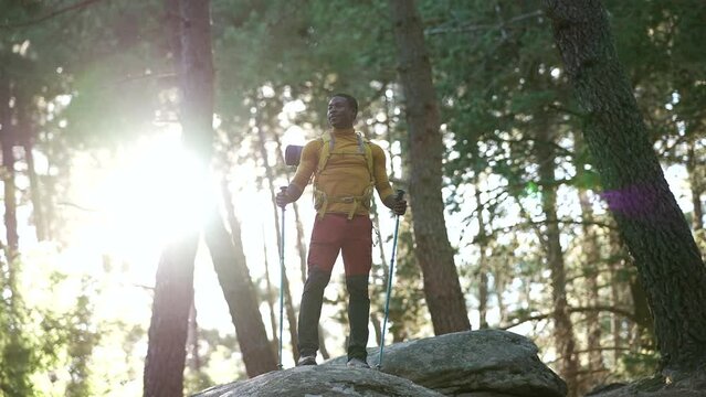 afro american man standing on a rock at sunset.Hiker or trail runner in mountains with backpack and poles