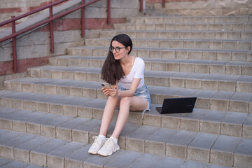 a girl with glasses is sitting on the stairs with a laptop on her lap