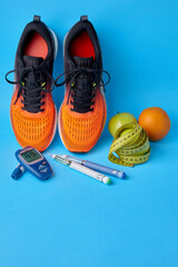 Orange sneakers, fruits, measuring tape, glucometer and insulin syringe pens on a blue background....