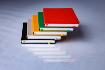 Colorful journals stacked together with a reflection. Beautiful studio photo of notebooks pens on white background. . High quality photo