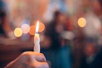 Woman holding a burning candle in a church for a ceremony. Bokeh candle lights in the background....