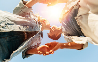 Obraz premium summer holidays, love and people concept - happy young couple holding hands under blue sky, from below