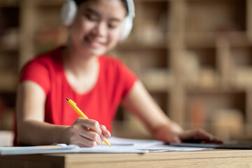 Glad happy adolescent asian lady student in wireless headphones studying in room interior, blurred, close up