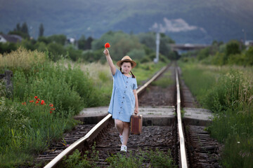 Fototapeta na wymiar A little girl in a dress walking on an abandoned railroad tracks