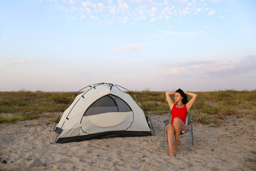 A beautiful girl is sitting on the beach next to a tent. Beach scene. Summer time. Weekend in outdoor. Summer camp.