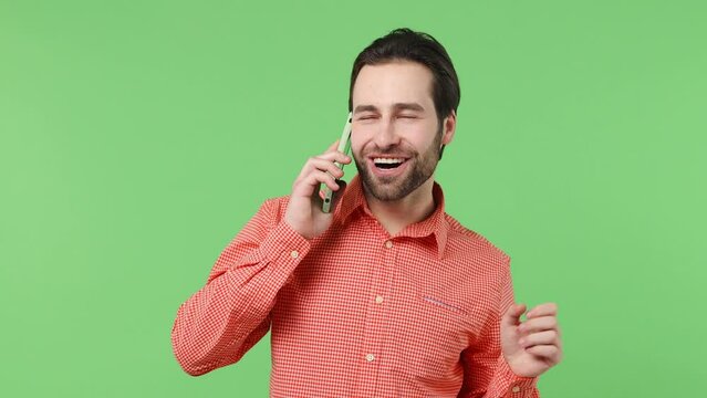 Happy calm exultant cheerful young brunet bearded man 20s years old wears pink shirt hold use talk on mobile cell phone conducting pleasant conversation isolated plain green background studio portrait