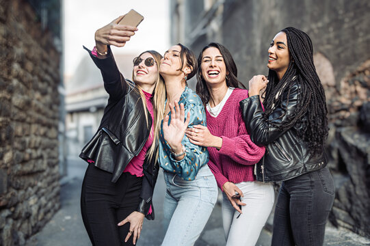 Four women best friends taking selfies on the street - generation z girls having fun outdoors taking pictures with their mobile cellphone - people, friendship and technology lifestyle concept