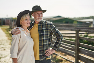 Senior farmer couple hug and look away on farm